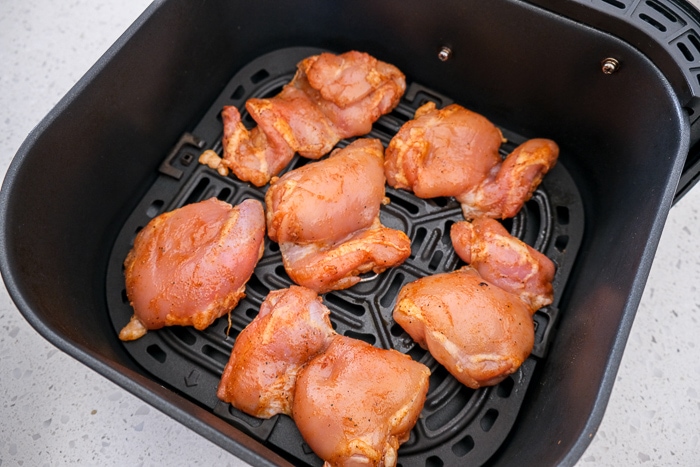 raw chicken thighs in black air fryer tray on counter top