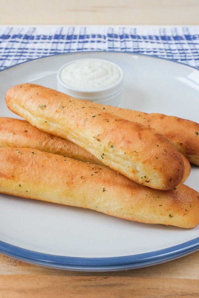 crispy breadsticks on large plate on wood with ranch dip behind