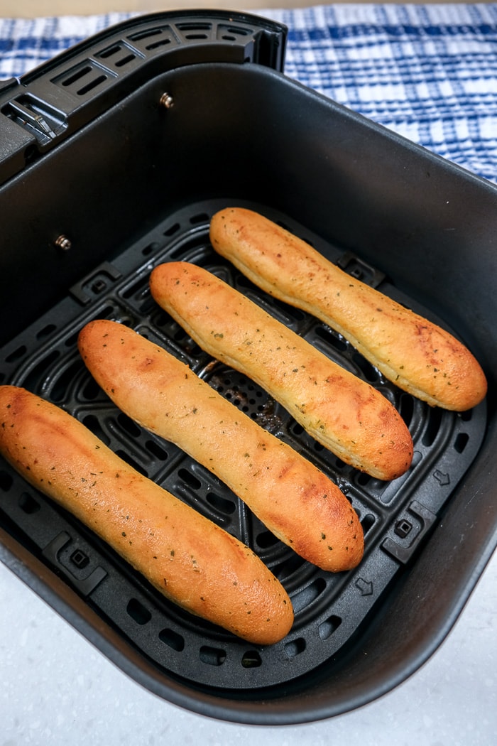 cooked breadsticks in black air fryer tray on counter top with blue cloth behind