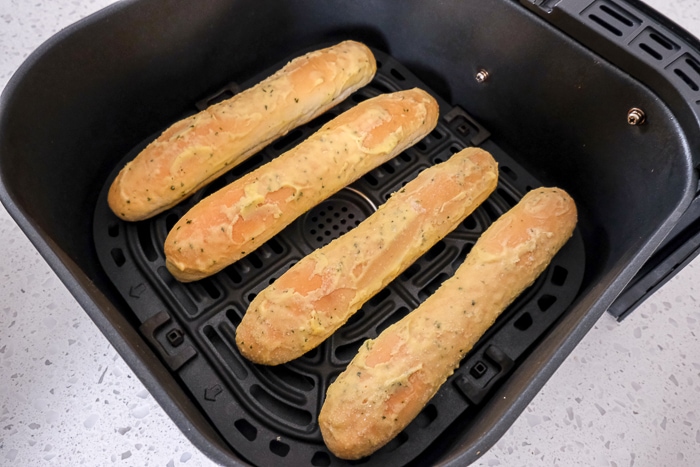 frozen breadsticks in black air fryer tray on white counter top