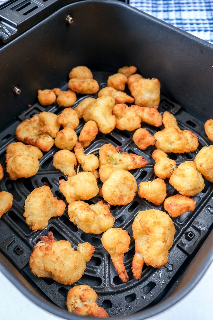 cooked cauliflower bites in black air fryer tray on white counter top with blue cloth behind