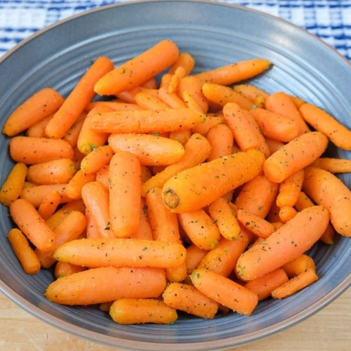 blue bowl of orange carrots on wooden board