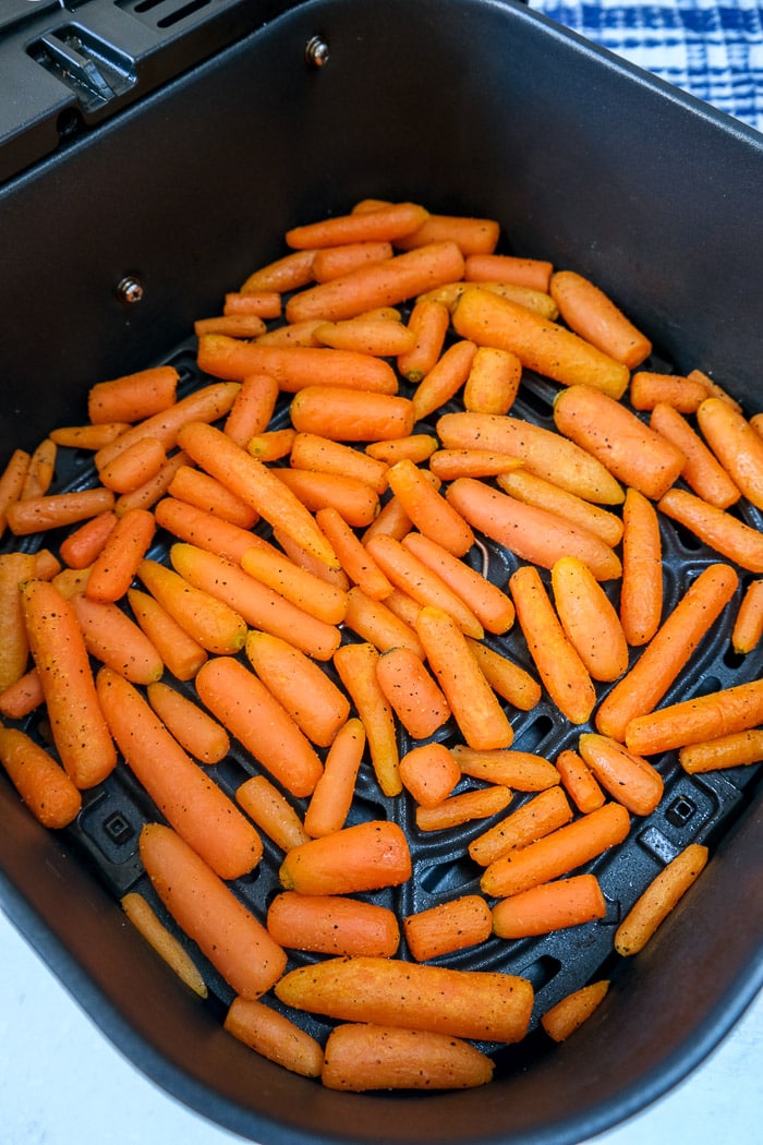 cooked baby carrots in black air fryer tray on blue counter