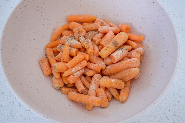 white mixing bowl full of frozen baby carrots and spices