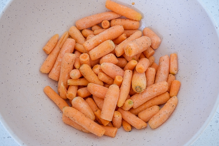 frozen baby carrots in mixing bowl on counter covered in spices