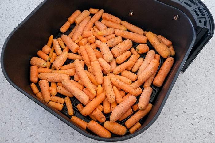 uncooked frozen carrots in black air fryer tray on white counter top