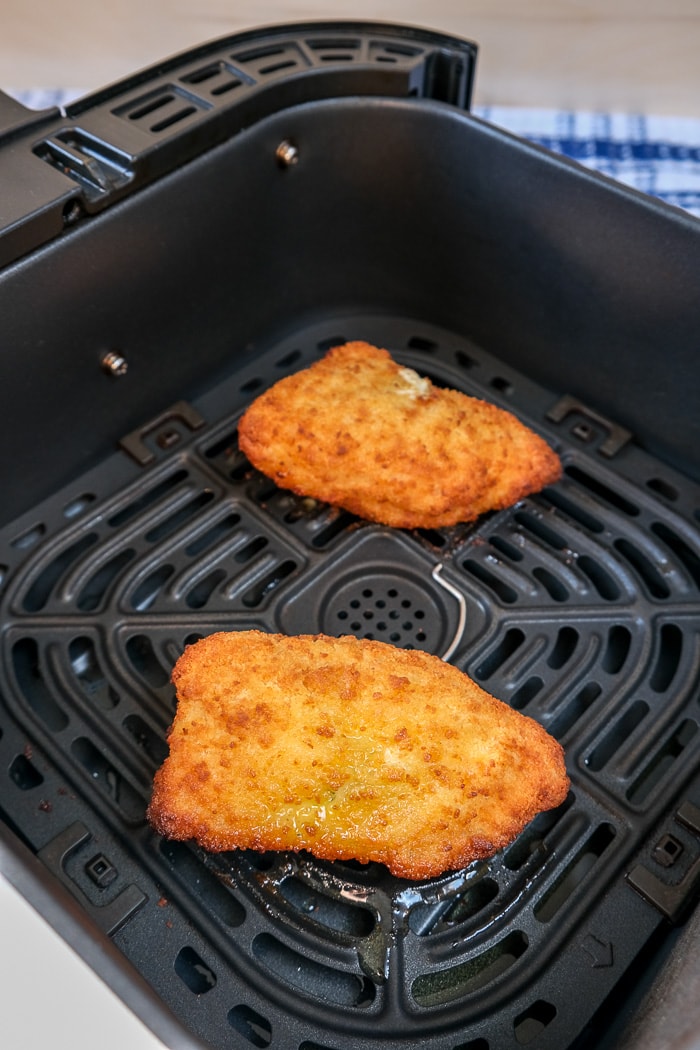 cooked breaded chicken kiev in black air fryer tray with blue cloth behind