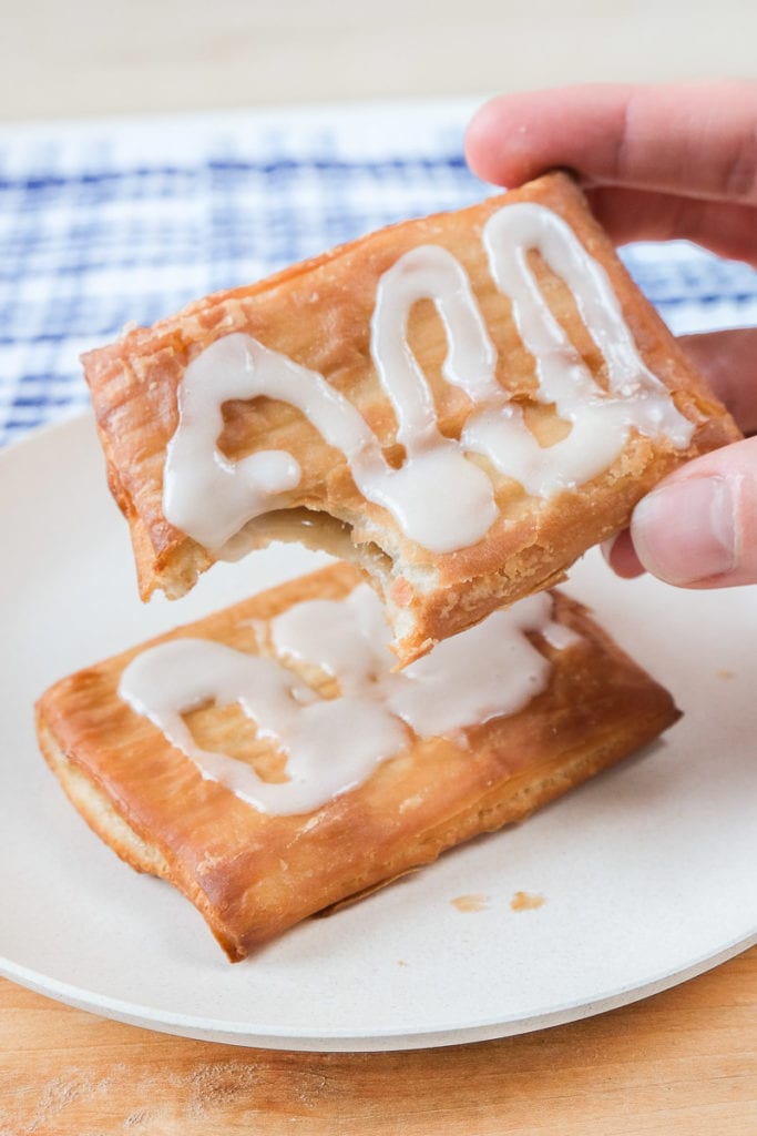toaster strudel held in hand with strudel on white plate behind