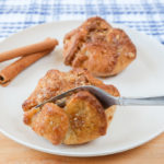 golden brown apple blossoms on white plate with metal fork cutting in half