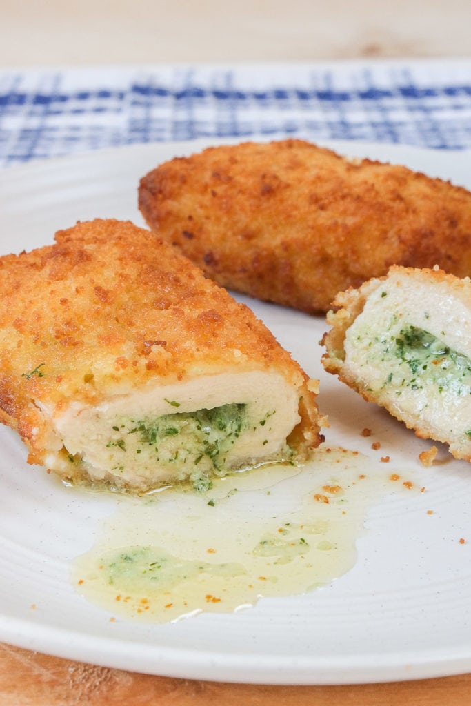 breaded chicken kiev cut open with herbs and butter spilling out on white plate