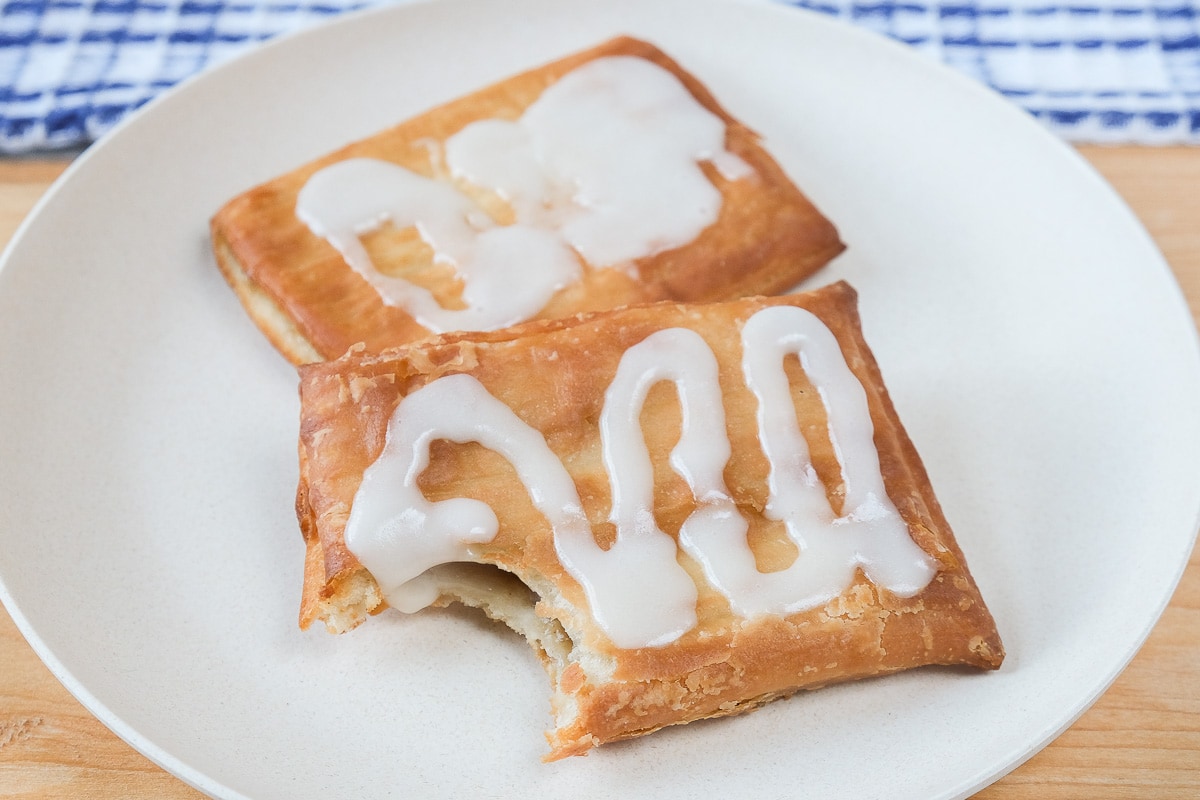 toaster strudel covered in icing on white plate on wooden board