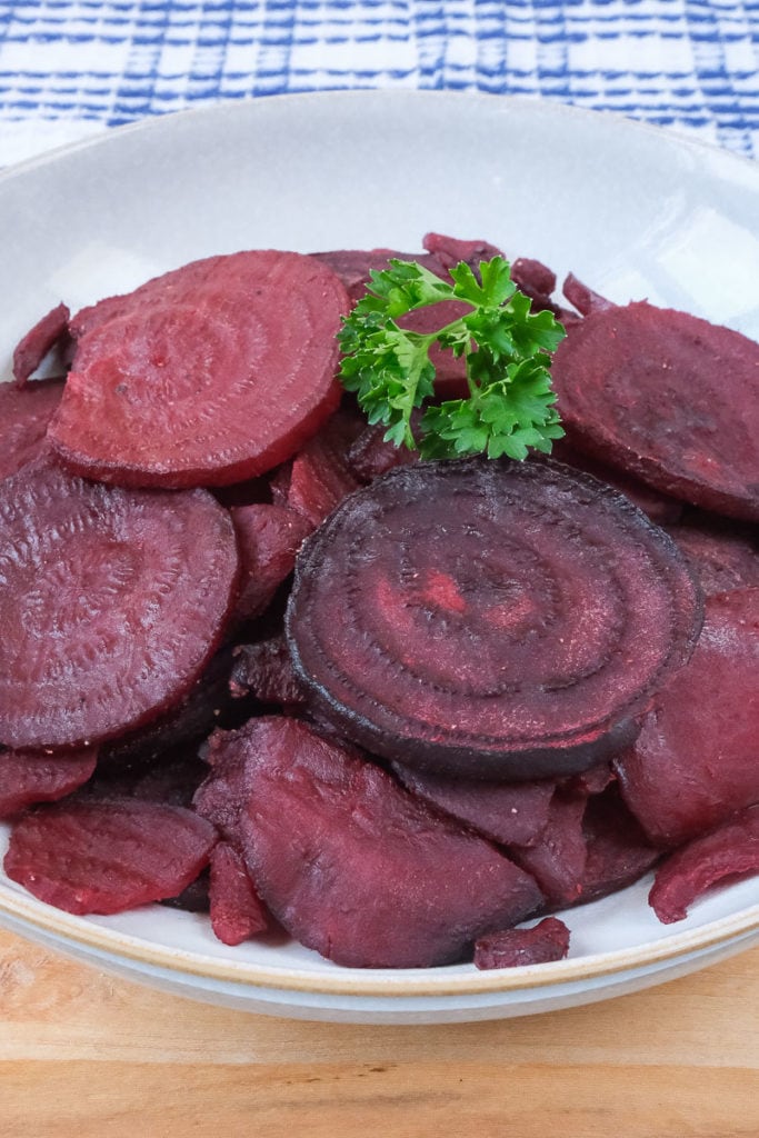sliced beets in bowl with green parsley on top sitting on wooden board