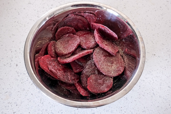 frozen beet slices in metal mixing bowl on white counter covered in spices.