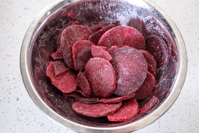 sliced frozen beets covered in spices in metal bowl on white counter.