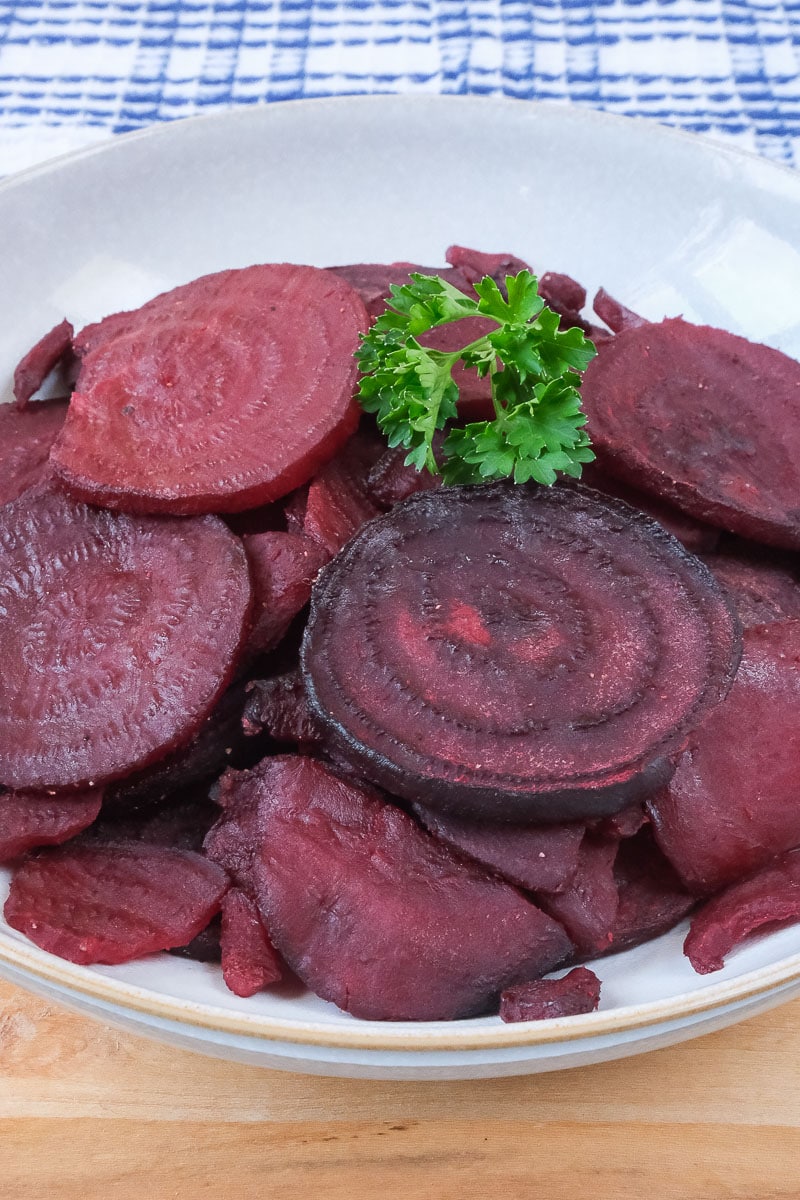 sliced beets in bowl with green parsley on top sitting on wooden board.