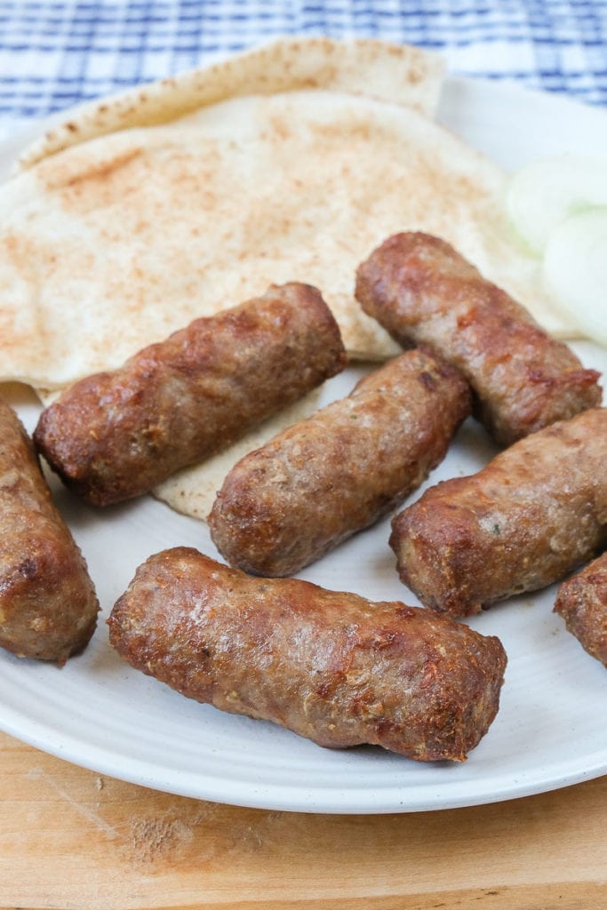 grilled sausages on white plate with pita and blue cloth behind.