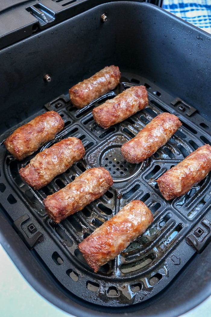 cooked cevapi sausages in black air fryer tray with blue cloth behind.