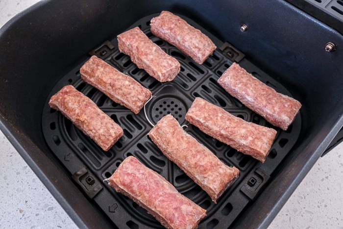 raw sausages in black air fryer tray on white counter top.