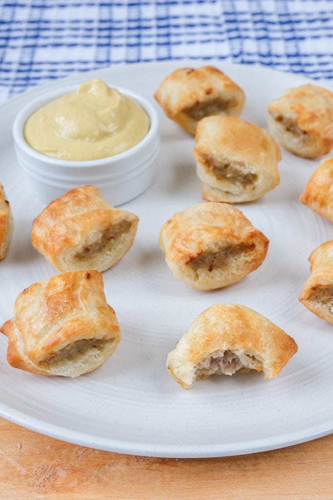 flakey sausage rolls on white plate with mustard dipping sauce beside