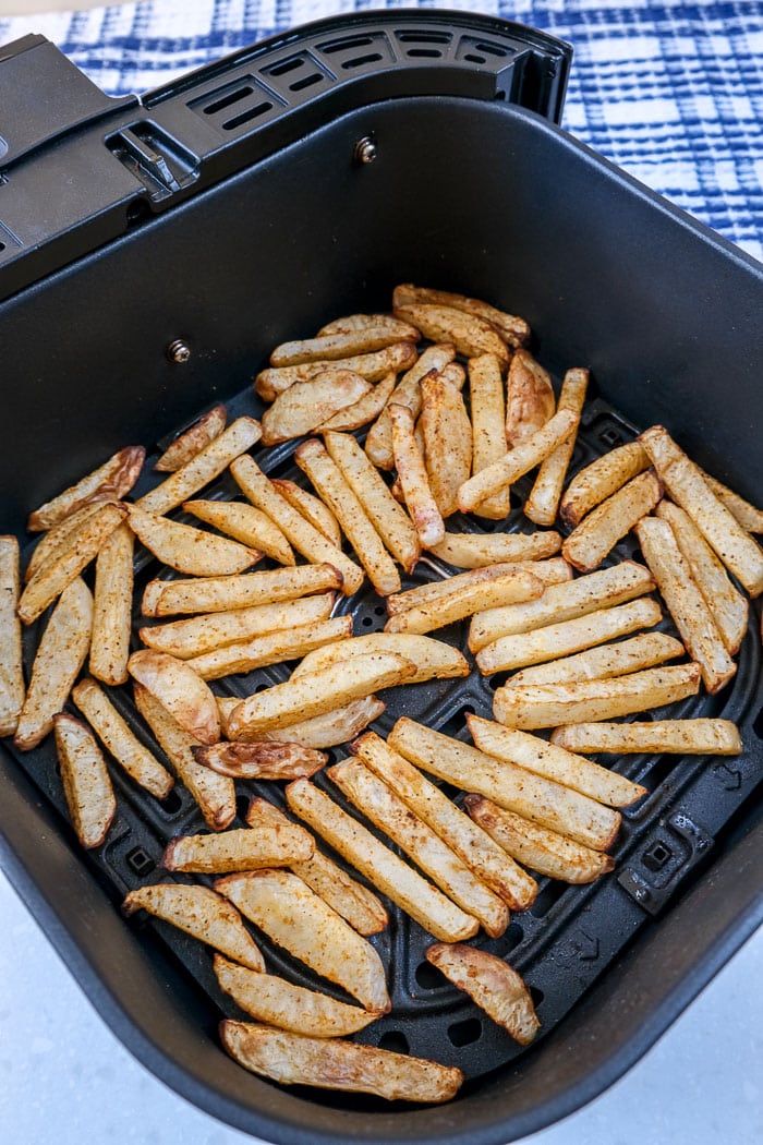 black air fryer full of cooked turnip fries with blue cloth behind.