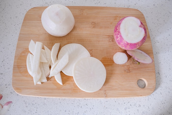 sliced turnip on wooden cutting board on white counter top.