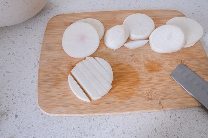 sliced raw turnip fries on wooden cutting board with knife beside.