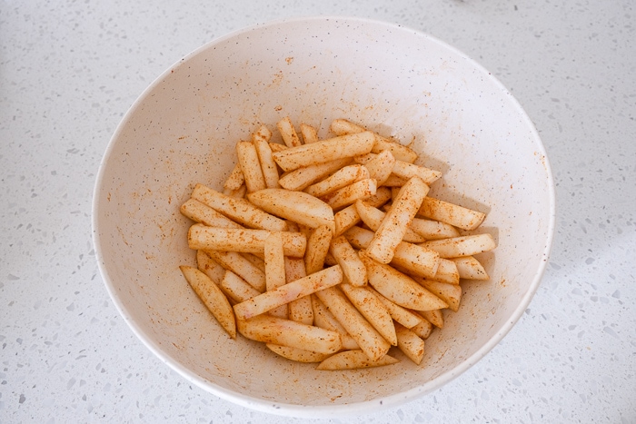 turnip fries coated in spices in white mixing bowl on counter.