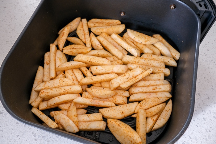 uncooked turnip fries in black air fryer tray on white counter.
