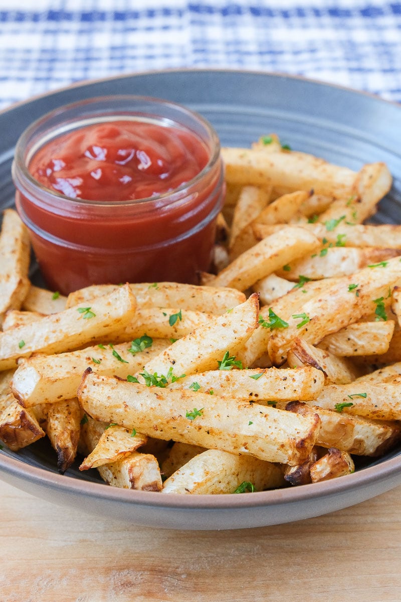 turnip fries in blue bowl on wooden board with ketchup for dipping beside.