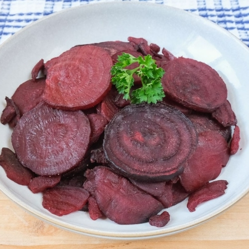 cooked sliced beets in bowl on wooden board with parsley on top