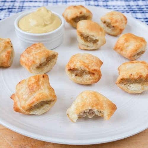 cooked sausage rolls on white plate with yellow mustard for dipping beside