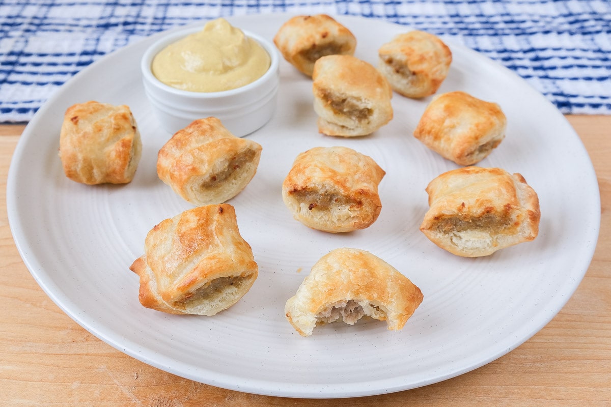 cooked sausage rolls on white plate with yellow mustard for dipping beside