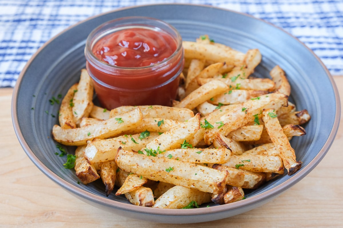 crispy turnip fries in blue bowl on wooden board with ketchup beside.