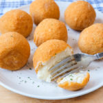 silver fork cutting arancini rice ball on white plate on wooden board.