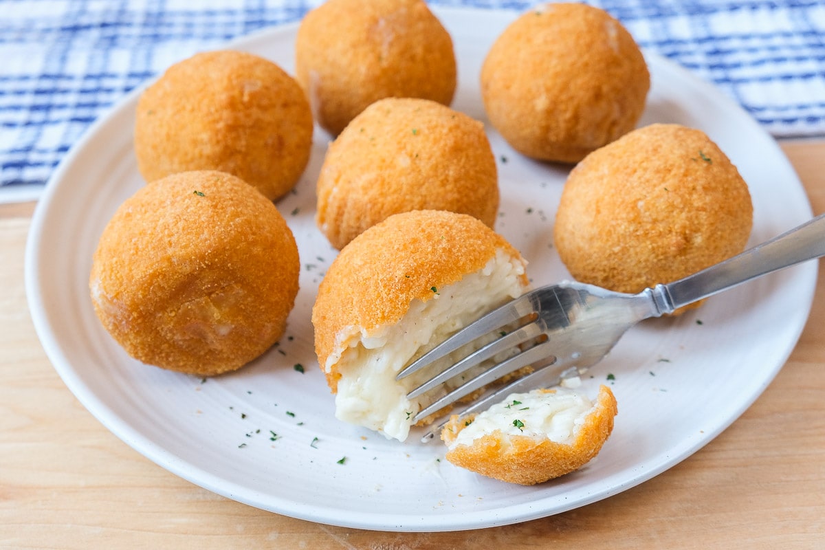 silver fork cutting arancini rice ball on white plate on wooden board.