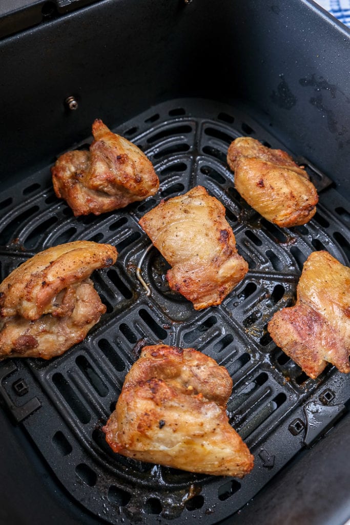 cooked chicken thighs on black air fryer tray.
