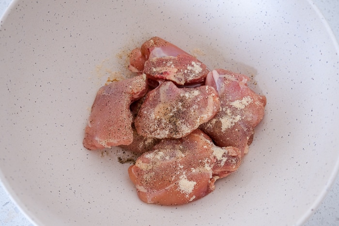 white bowl of raw chicken thighs covered in spices.