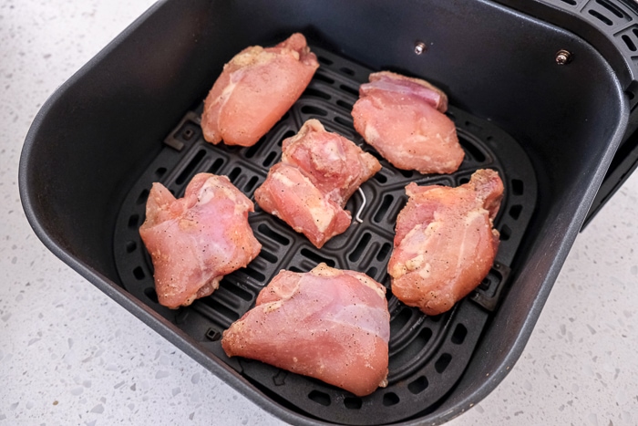 raw chicken thighs in black air fryer tray on white countertop.