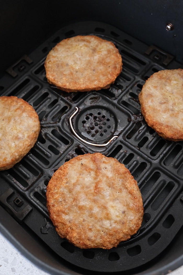 cooked sausage patties in black air fryer tray on white counter top.