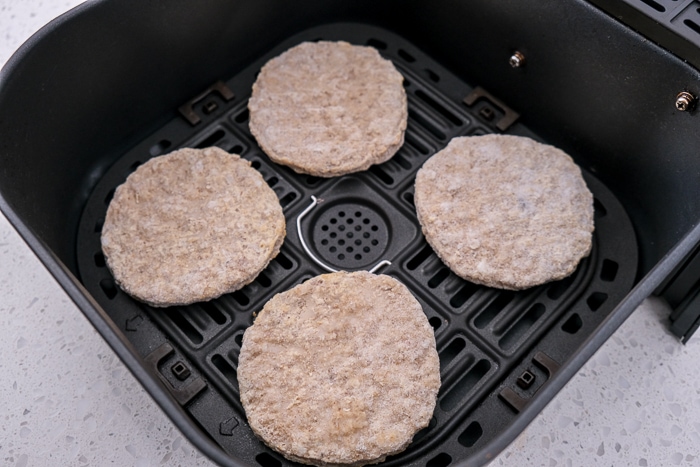 frozen sausage patties in black air fryer tray on white counter.
