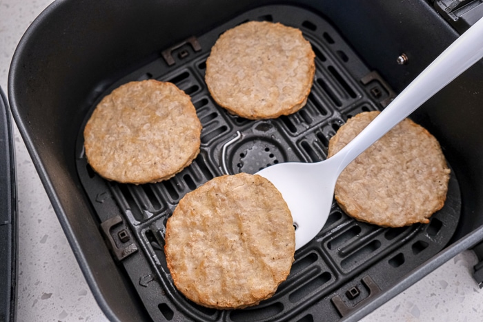 white flipper flipping cooked sausage patty in black air fryer tray.