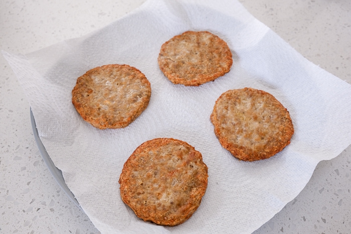 four cooked sausage patties on white paper towel on place on white counter.