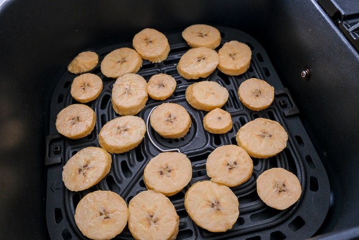 uncooked plantain chips in black air fryer tray.