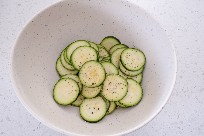 slices of zucchini in white bowl on white counter top.
