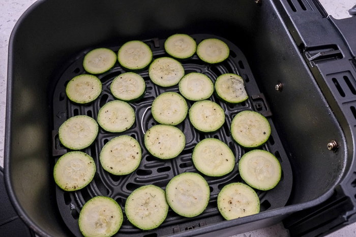 raw zucchini chips in black air fryer tray on counter top.