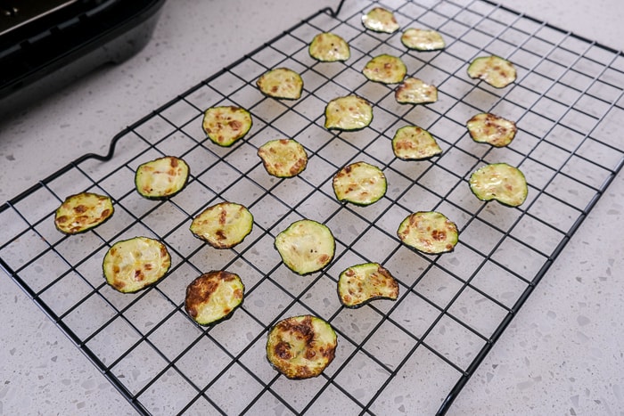 cooked zucchini chips on cooking rack on white counter top.