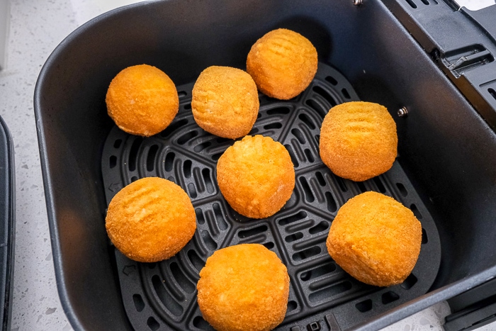 frozen arancini rice balls in black air fryer tray on white counter top.
