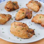 crispy chicken thighs on white plate with chopped parsley on top.