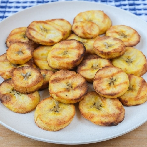 crispy plantains on white plate on wooden board with cloth behind.
