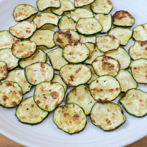 crispy zucchini chips on white plate on wooden board.
